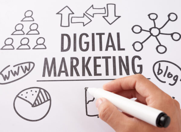 From above shot of crop hand using marker pen to draw icons near digital marketing writing on paper sheet